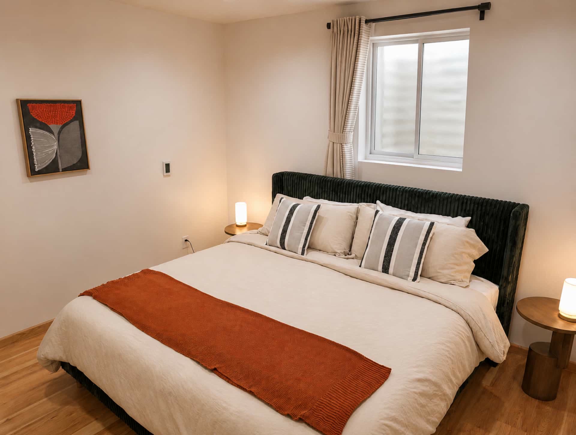 King bedroom with a dark upholstered headboard, a rust bed runner, candles, and a window to the trees.