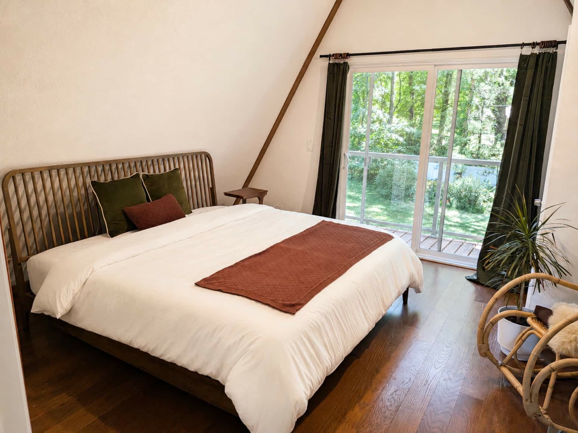 King bedroom with warm wood floors and sliding glass doors opening to green trees and the deck.
