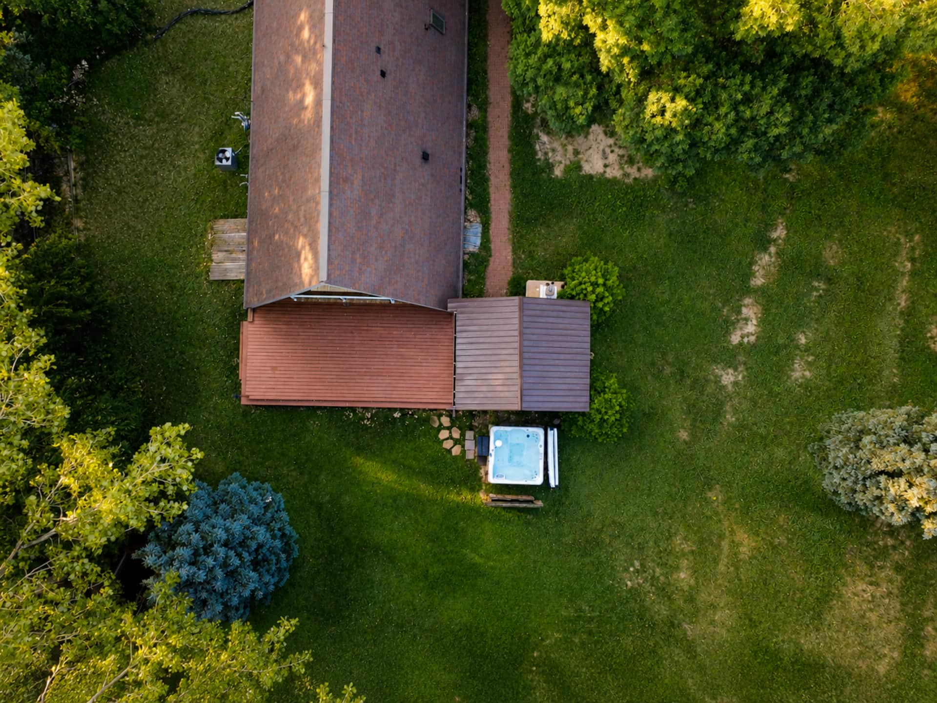 Aerial view of the A-frame from above, showing its roof, deck, and hot tub surrounded by an acre of green wooded grounds.